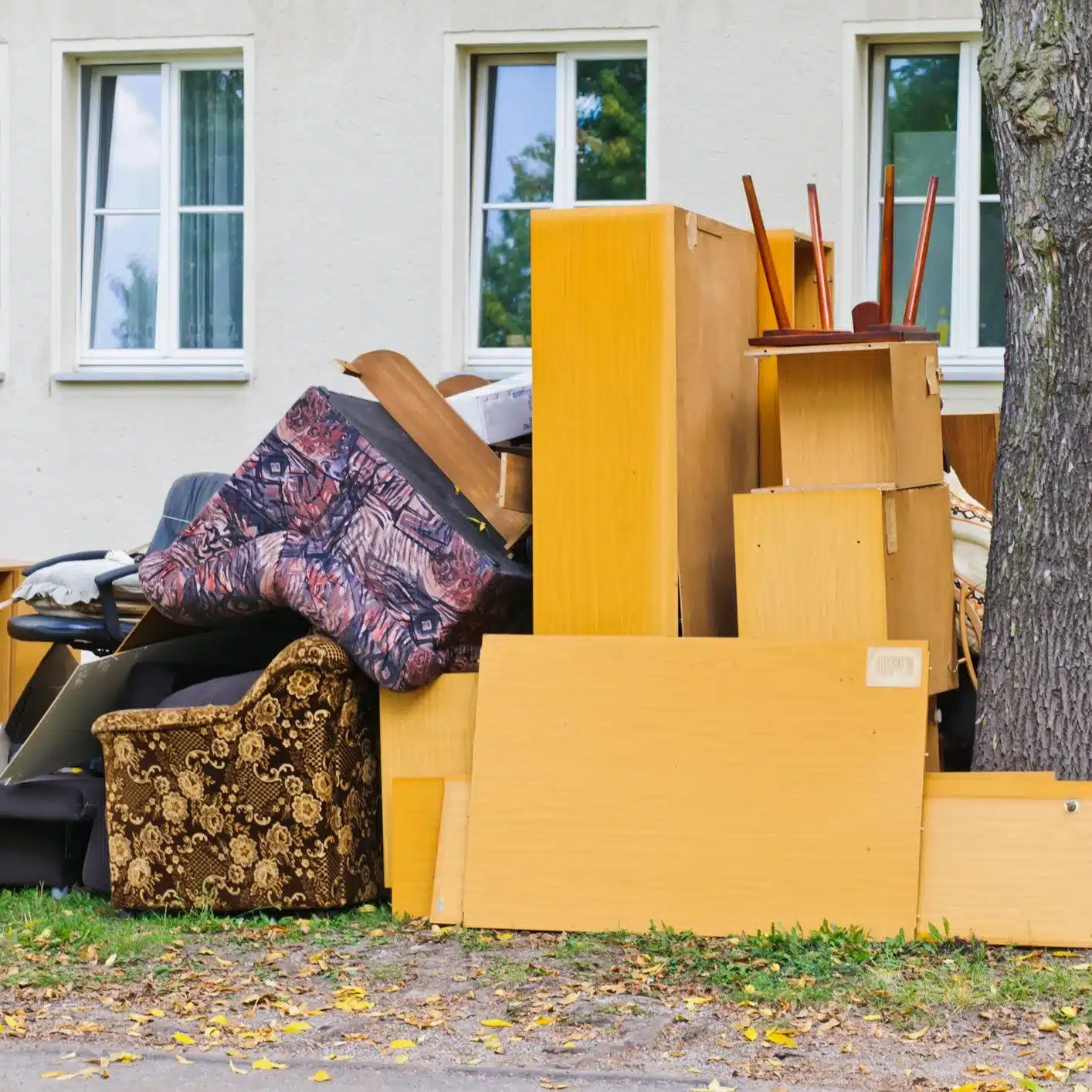 Household rubbish outside of a house, near a tree.